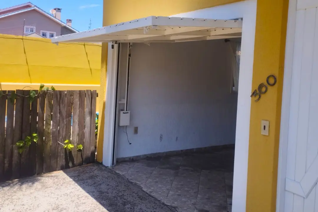 Portão basculante branco de elevação automatizado em residência, mostrando a calha lateral e o motor de contrapeso.